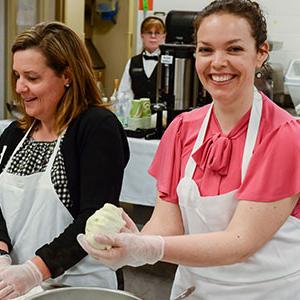 Woman in pink smiling at camera as she prepares food